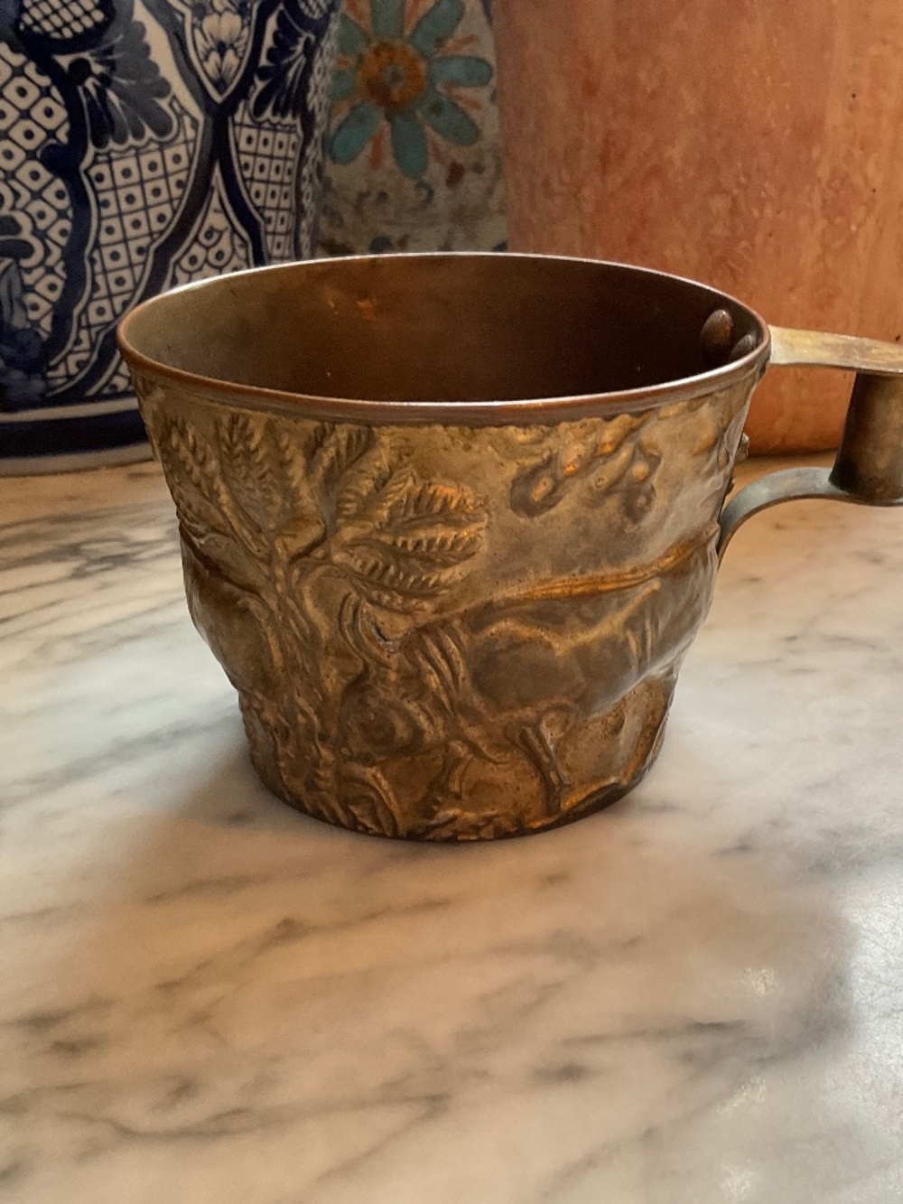 Antique brass handled cup with animal relief on exterior